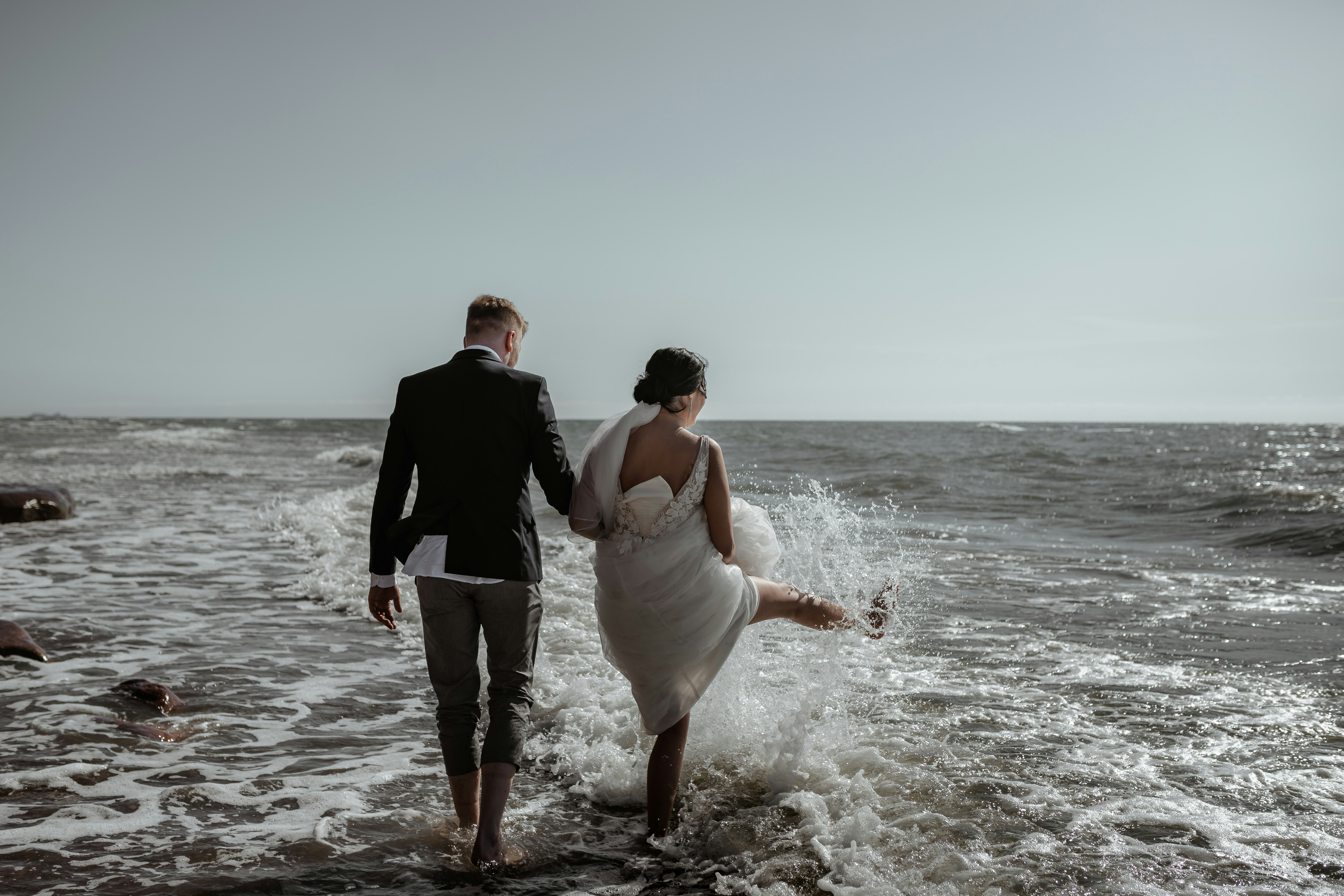 man in black suit holding woman in white dress on beach during daytime